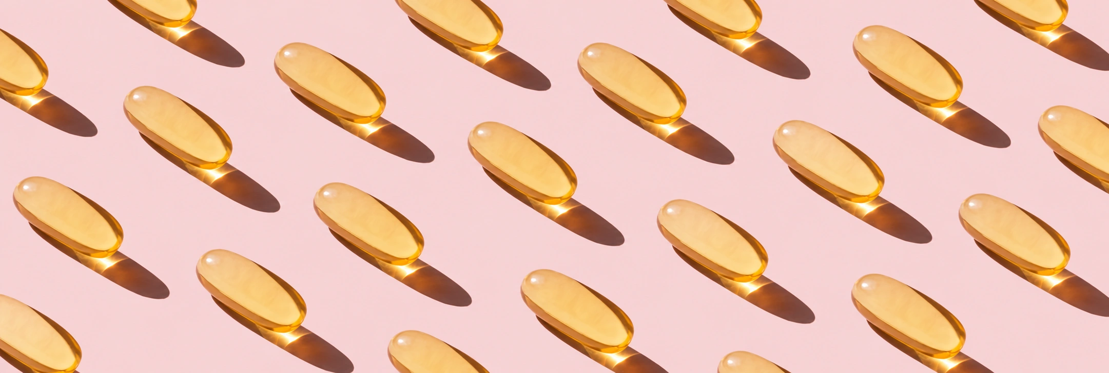 Golden softgels on a soft pink background